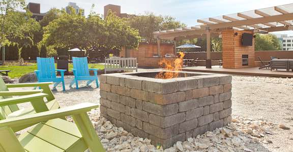 A fire pit is in the middle of a gravel area with blue and green chairs around it.