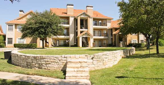 a stone retaining wall in front of an apartment building at The Olivine in North Austin, TX