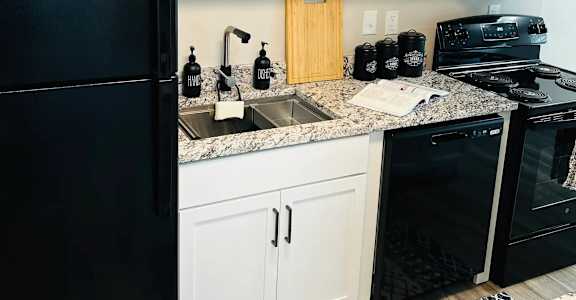 A black refrigerator stands next to a sink in a kitchen at Eton Square Apartments and Townhomes, Michigan, 48009