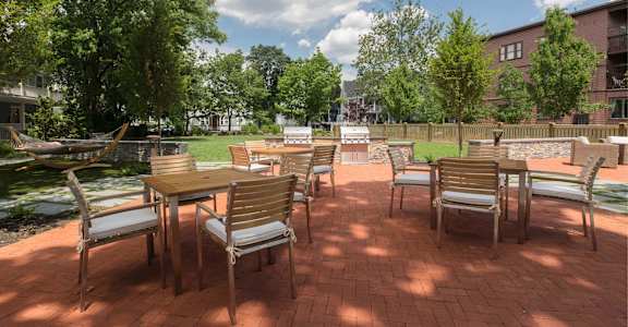 A patio with chairs and a table is surrounded by trees.