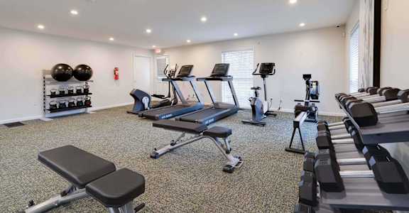 a gym with treadmills and weights in a room with windows at Station JTown, Louisville, KY, 40299