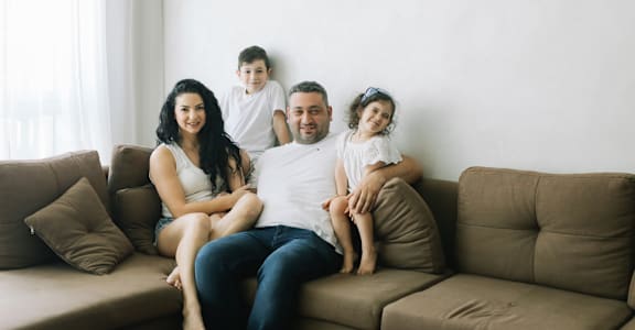 A family of four is sitting on a brown couch.at Northside Hills Apartments, Griffin Georgia