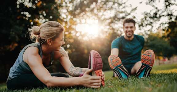 A man and a woman are sitting on the grass, stretching their legs.