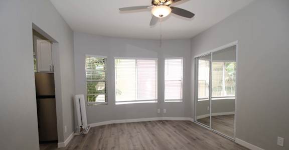 an empty living room with a ceiling fan and windows