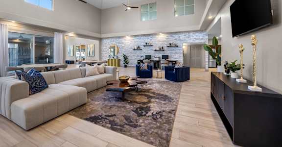 A spacious living room with a large sectional sofa, a coffee table, and a flat-screen TV mounted on the wall.