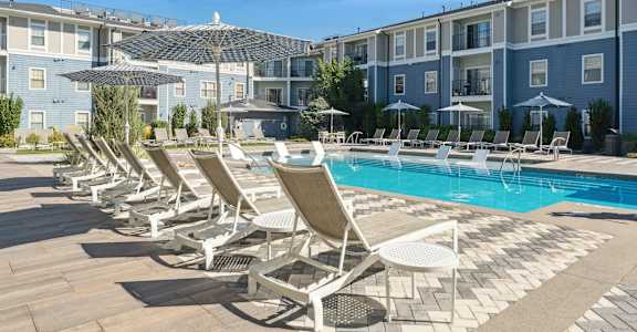 A row of sun loungers are set up on a wooden deck next to a swimming pool.