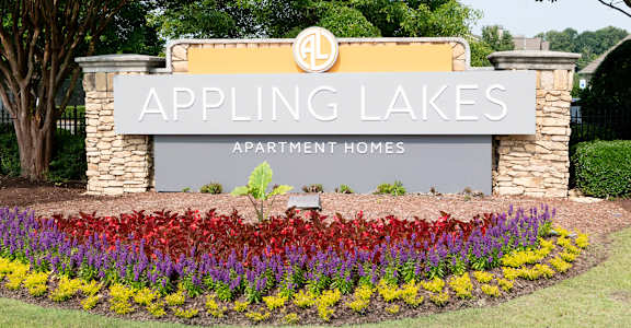 A sign for Appling Lakes Apartment Homes is surrounded by flowers.