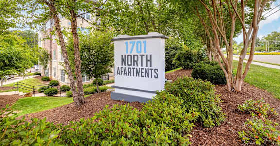 A sign for 1701 North Apartments is surrounded by green shrubbery and trees.
