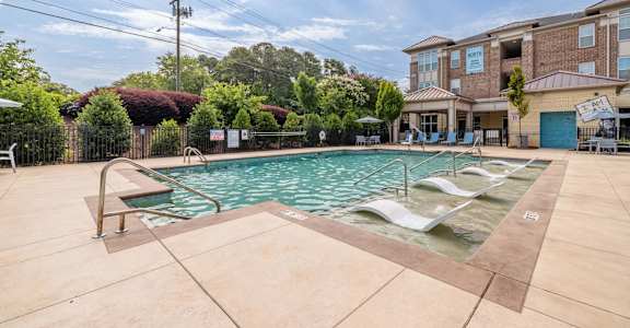 A large outdoor swimming pool with lounge chairs and a building in the background.