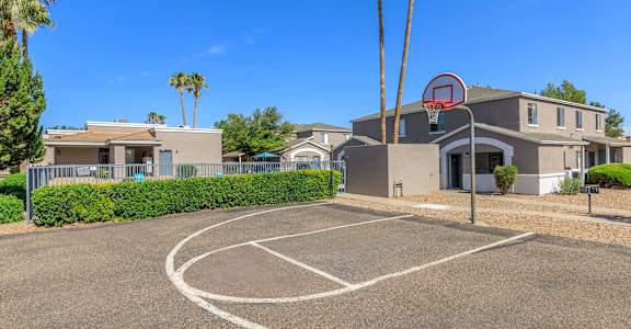 A basketball court is located in front of a building with a basketball hoop mounted on it.