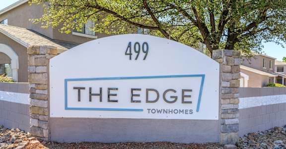 A sign for "The Edge" townhomes stands in front of a building.