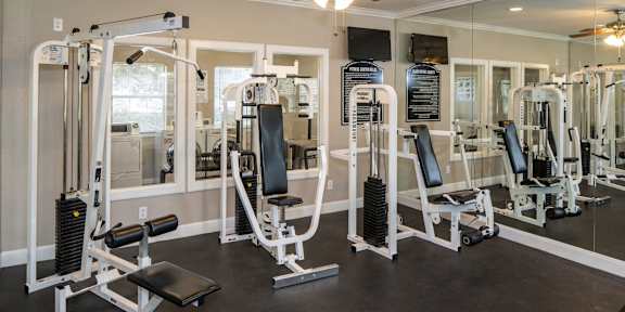 A gym with a variety of equipment including a squat rack, bench press, and a mirror. at Infinity on Sunnyvale Apartments , Mesquite, 75150