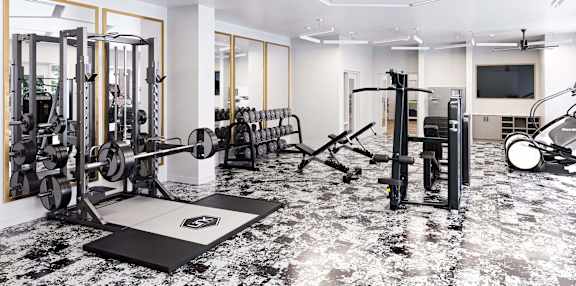 a gym with weights and a tv on the wall and a marble floor at Link Apartments® Calyx, North Carolina