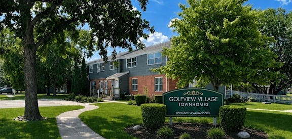 A sign for Golfview Village Townhomes is in the foreground of a well kept lawn.