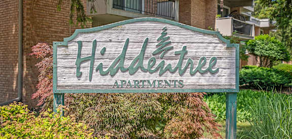 A sign for Hidden Tree Apartments is displayed in front of a building.