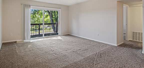 A spacious room with a carpeted floor and sliding glass doors leading to a balcony.