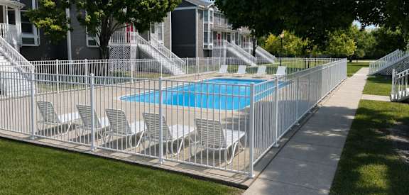 A pool surrounded by a metal fence with chairs on it.