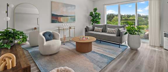 A living room with a grey couch, a blue rug, and a painting on the wall.