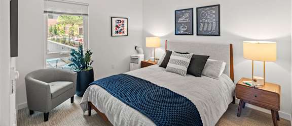 A bedroom with a bed, chair, and two lamps.