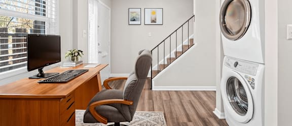 A washing machine is placed in a room with a desk and a chair.