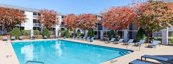 A large swimming pool surrounded by lounge chairs and trees.