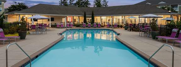 A large swimming pool surrounded by purple chairs and umbrellas.