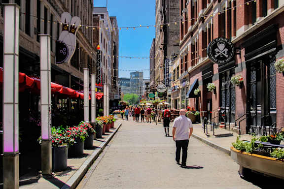A man is walking down a street lined with flower pots and storefronts.