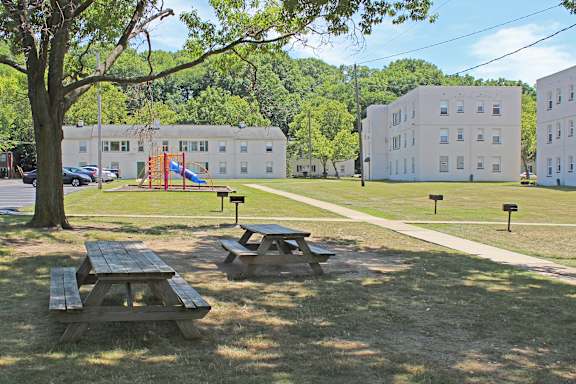 A playground with a slide and picnic tables in the foreground with buildings in the background.
