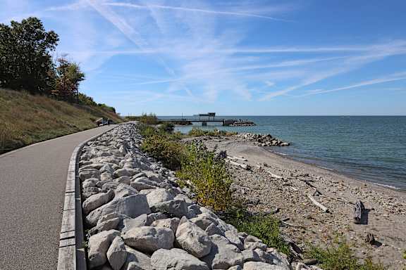 A paved path runs along a rocky beach next to a body of water.