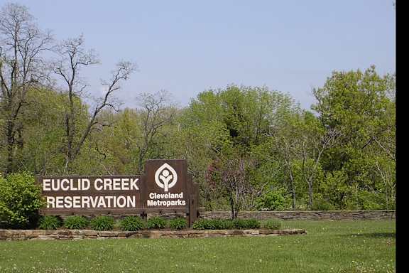 A sign for Euclid Creek Reservation stands in a field of grass.
