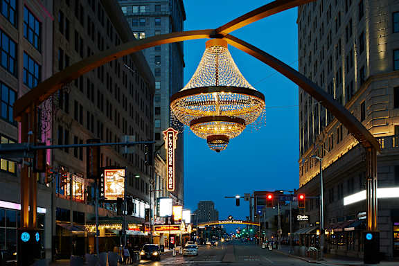 A street view of a city with a large hanging light fixture in the foreground.