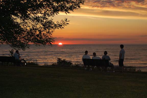 A group of people are sitting on a bench watching the sunset by the ocean.
