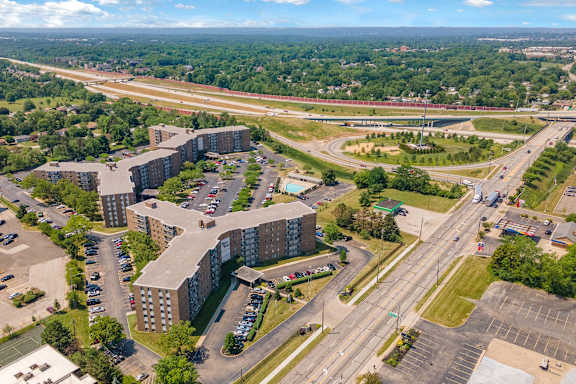 A large building complex is surrounded by a parking lot and a highway.