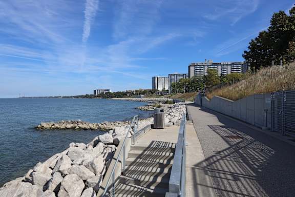 A walkway next to a body of water with rocks and a building in the background.