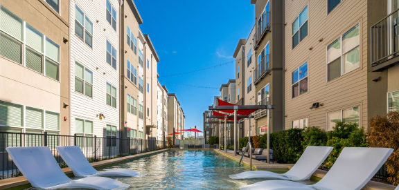 a swimming pool between two apartment buildings with white chairs