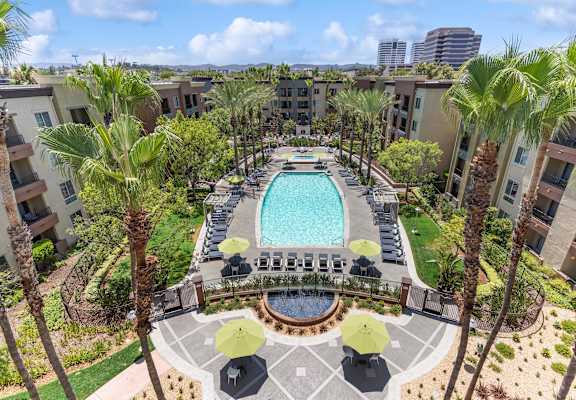 A pool surrounded by palm trees and umbrellas. at The Kitt at Warner Center Apartments, Woodland Hills, CA