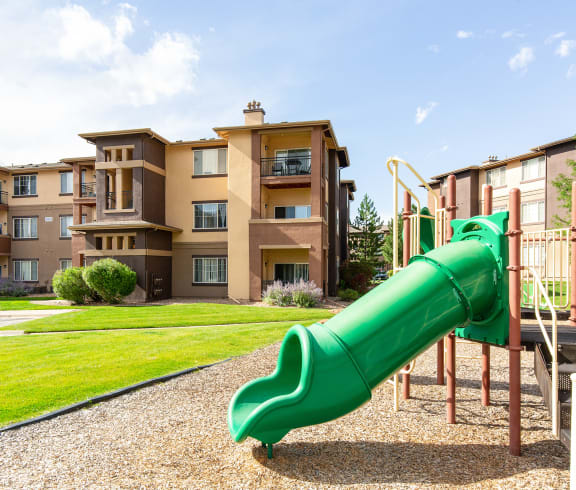 a green slide in the middle of a grassy area in front of an apartment complex