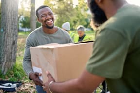 a man handing a box to a friend in a park