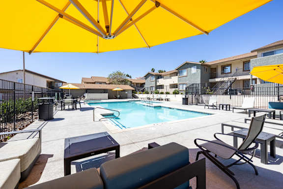 A swimming pool in front of a building with a yellow umbrella and chairs.