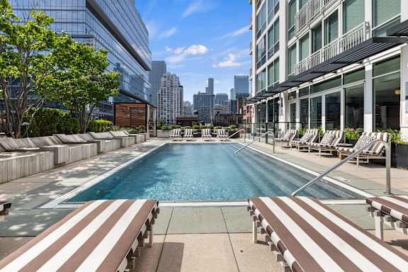 A large swimming pool with brown and white striped lounge chairs.