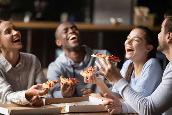 Four people laughing and eating pizza together.