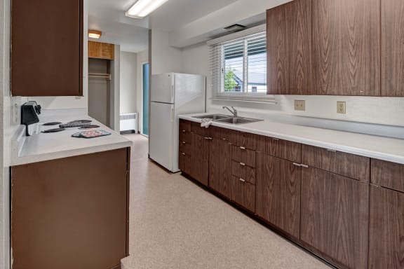 A kitchen with wooden cabinets and a sink and a refrigerator at Bay Arms Apartments. 