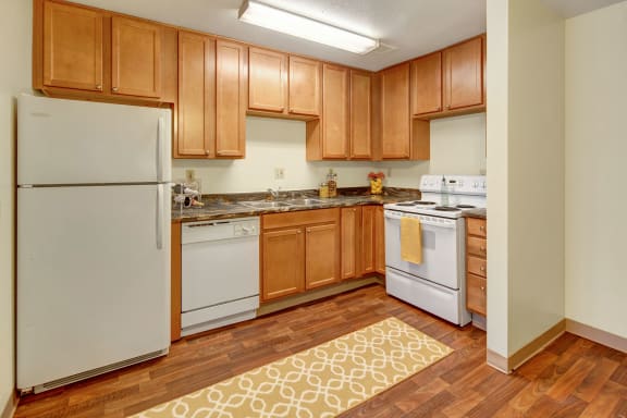 A kitchen with wooden cabinets and marble countertops at Conifer Grove. 