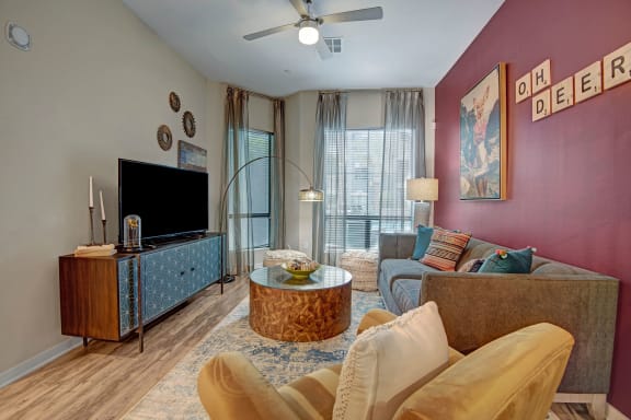 The living room with a couch, plush chairs, coffee table, decorations, a TV, and windows with sheer curtains at Park on Central Apartments. 