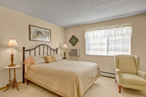 A bedroom with a queen-size bed, a chair, decorations, window, and nightstands at Heritage Park.
