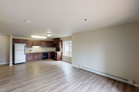 A large empty living room with hardwood flooring and kitchen with a door to a balcony at Renaissance Heights Apartment Homes. 