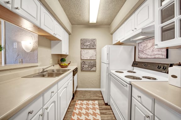 A kitchen with white appliances and counters at Brookwood Village Apartments. 