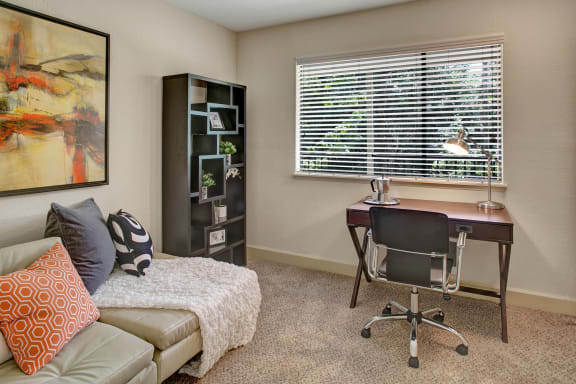 An office with a couch, window, bookshelf, and artwork at Heritage Hills. 