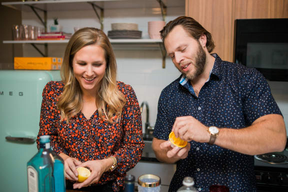 a man and woman in a kitchen peeling an orange