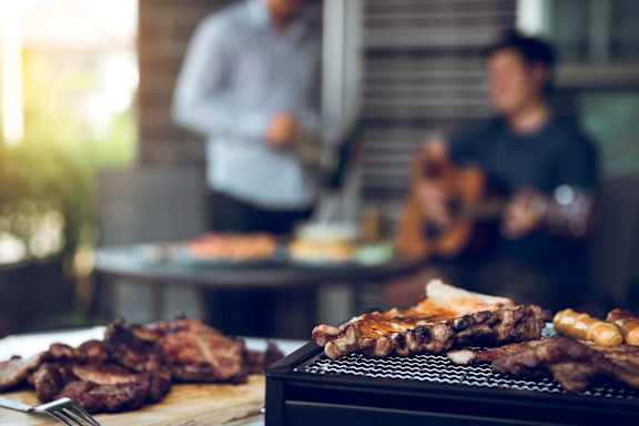 A man is grilling meat while another man plays guitar in the background.at The Residences at The Gilmore in Gilbert, AZ